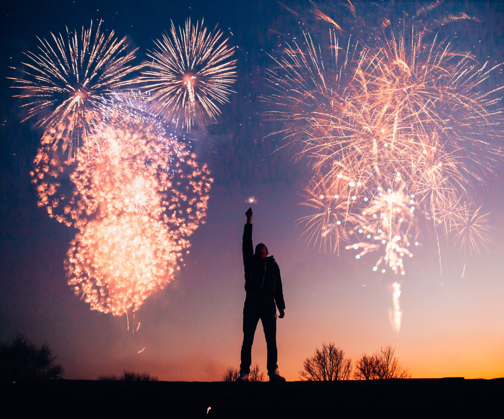 man holding a candle with fireworks behind them - event clothing